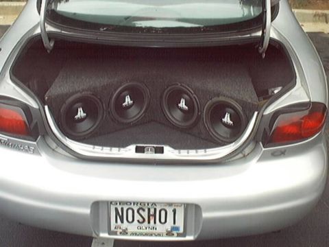 1998 Ford Taurus - Rear view of a silver sedan with the trunk open, showing a custom audio install with four JL Audio subwoofers mounted in a carpeted enclosu…