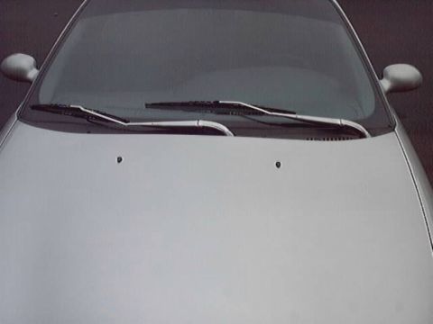 1998 Ford Taurus - Tight head-on view across the hood and windshield of a silver sedan, showing the twin wiper arms parked at the cowl, washer nozzles on the…