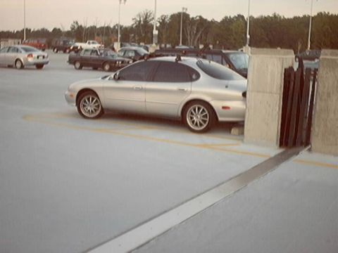 1998 Ford Taurus - Silver Ford Taurus sedan parked on the top deck of a concrete parking garage, shown in profile with aftermarket multi-spoke alloy wheels an…