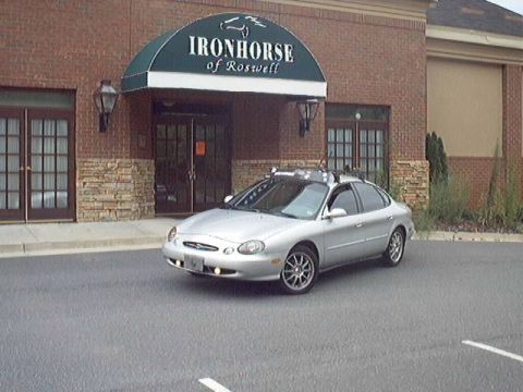 1998 Ford Taurus - Silver Ford Taurus sedan parked at a front three-quarter angle outside a brick building with a green 'Ironhorse of Roswell' awning. The car…