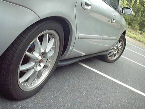 1998 Ford Taurus - Low-angle side view of a silver Ford Taurus sedan focused on the rear wheel, fitted with a multi-spoke silver aftermarket wheel showing a r…
