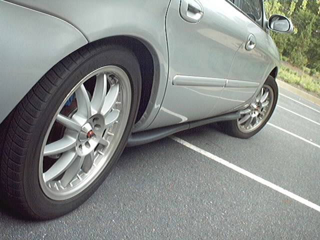 Silver sedan rear wheel with multi-spoke wheel and blue caliper, parked on asphalt