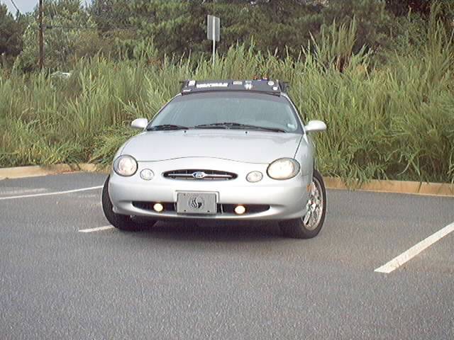 Front view of silver Ford Taurus sedan with roof light bar in a parking lot