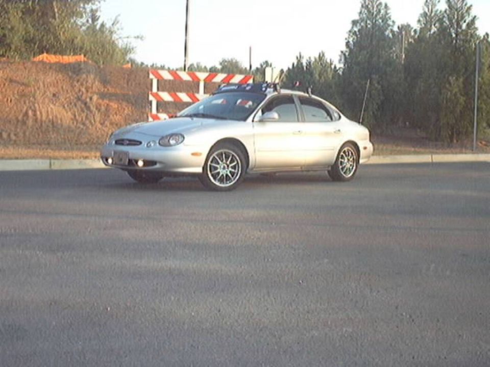 Silver Ford Taurus sedan on new pavement near a construction barricade