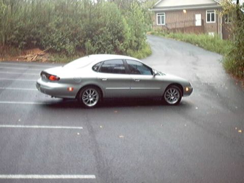1998 Ford Taurus - Silver 1998 Ford Taurus parked on a wet road next to a house.