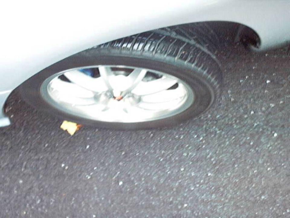 Close-up of a car's front wheel and fender. A yellow leaf is on the ground near the tire