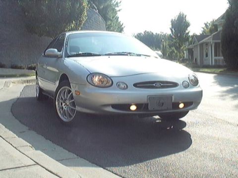 1998 Ford Taurus - A silver sedan is parked on a street with houses in the background.