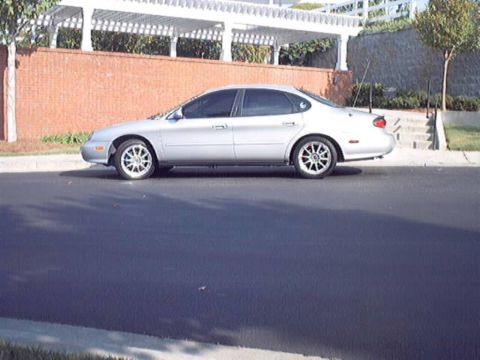1998 Ford Taurus - A silver 1998 Ford Taurus sedan is parked on the side of a road.