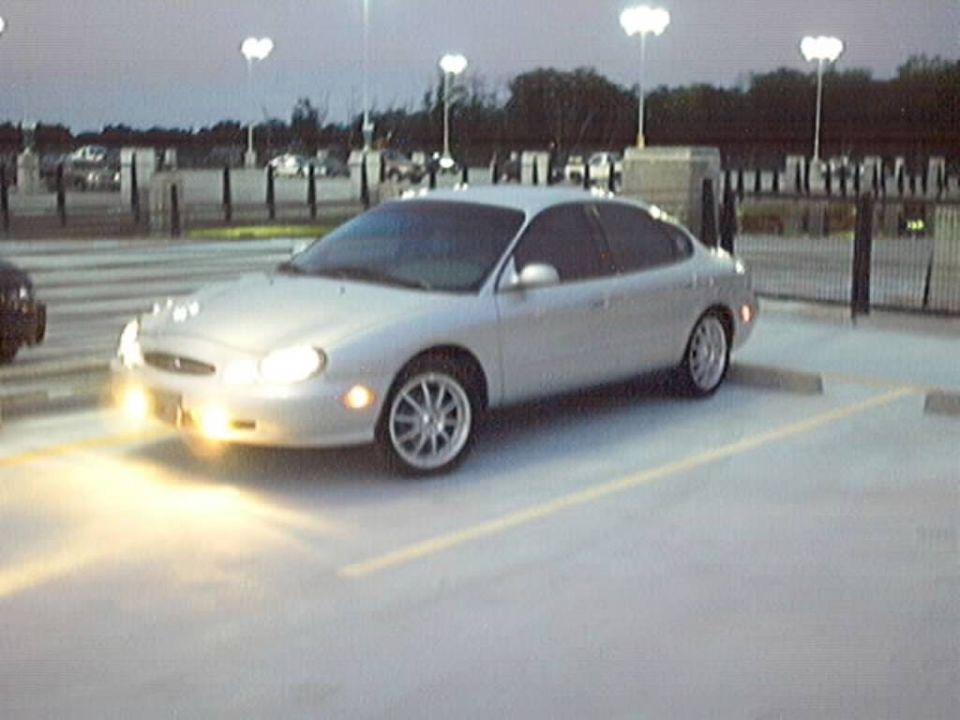 Silver sedan parked in a lot at dusk. Headlights are on