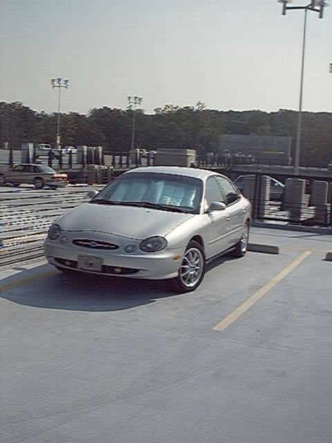 1998 Ford Taurus - A silver sedan is parked in an outdoor lot under a bright sky.