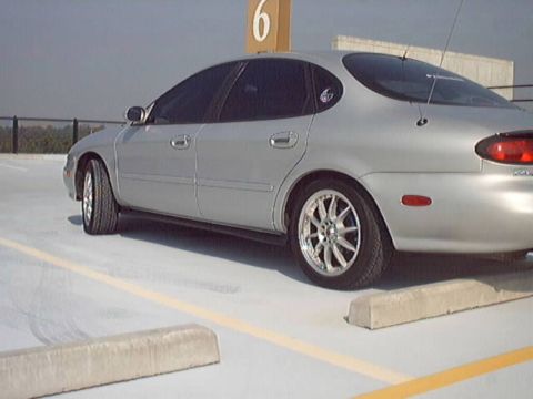 1998 Ford Taurus - A silver sedan is parked in a lot with a yellow line on the ground and concrete stoppers.