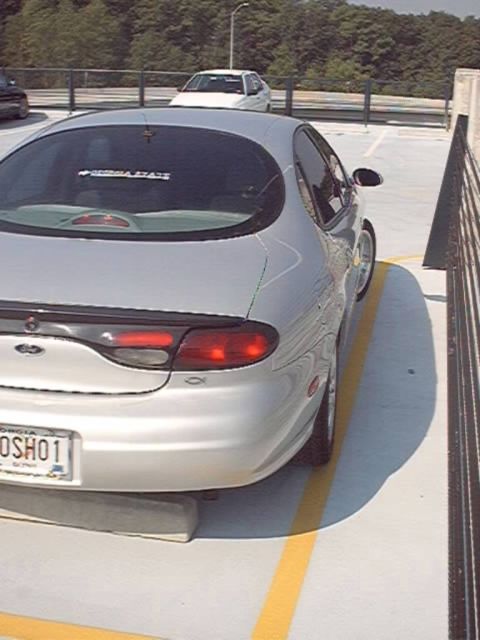 1998 Ford Taurus - Silver Ford Taurus sedan parked nose-in on the top deck of a parking garage, shot from a raised three-quarter rear angle showing the oval t…