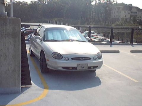 1998 Ford Taurus - A white sedan is parked in a lot, with a Ford emblem visible on its front grille.