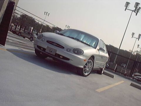 1998 Ford Taurus - A silver 1998 Ford Taurus sedan is parked in a lot, viewed from the front three-quarter angle.