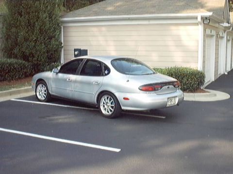 1998 Ford Taurus - A silver 1998 Ford Taurus is parked in a lot next to a building.