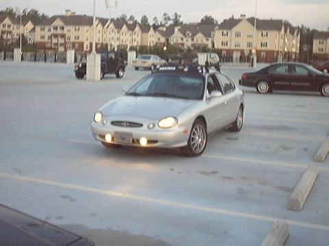 1998 Ford Taurus - Silver 1998 Ford Taurus sedan with a roof rack is seen from the front in a parking lot.