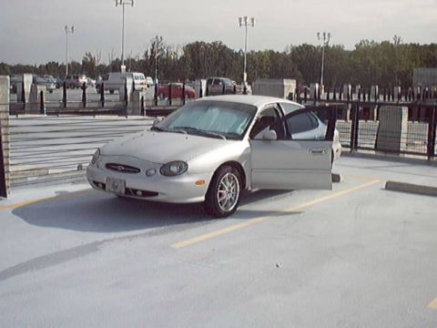 1998 Ford Taurus - A silver sedan is parked in a lot with its driver's door ajar, showing the interior.