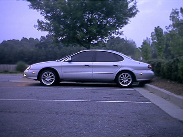 Silver Ford Taurus sedan side profile at dusk in an empty parking lot