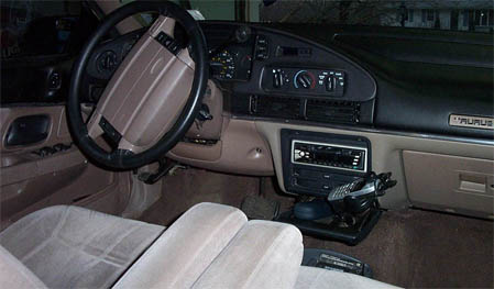 1993 Ford Taurus - The interior of a 1993 Ford Taurus shows beige cloth seats and a tan dashboard with a black steering wheel.