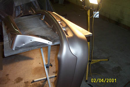 1993 Ford Taurus - A car bumper rests on a table under a bright work light in a garage.