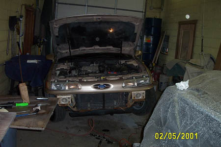 1993 Ford Taurus - Front view of a gold Ford Taurus with its hood up, showing the engine bay and a disassembled front bumper.