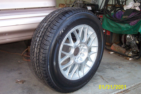1993 Ford Taurus - A newly mounted tire on a silver multi-spoke mesh alloy wheel standing upright on a garage floor, with the center cap missing to reveal the…