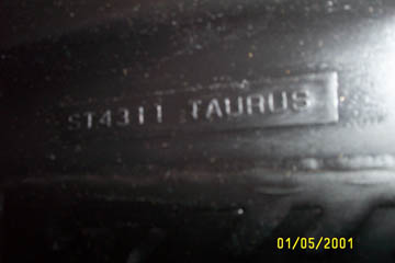 1993 Ford Taurus - Close-up of a molded part number stamped into a black plastic component, reading "ST4311 TAURUS" in raised lettering on a recessed panel. C…