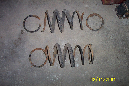 1993 Ford Taurus - Two worn coil springs, likely from a vehicle's suspension, lie on a concrete floor.