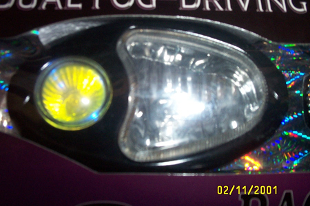 1993 Ford Taurus - Close-up of aftermarket driving lamps still in their retail packaging, showing an oval clear lens beside a small round yellow lens on a bla…