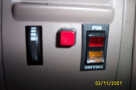 1993 Ford Taurus - Close-up of an aftermarket switch panel mounted in a tan interior trim panel, with a slider-style dimmer control, a square red rocker butto…