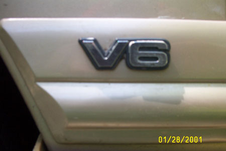 1993 Ford Taurus - Tight close-up of a chrome "V6" emblem mounted above the body-side molding on a champagne/gold painted body panel. Camera date stamp reads…