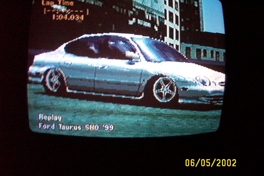 TV screen showing a video game replay of a silver Ford Taurus SHO sedan