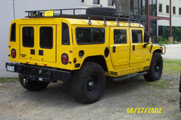 1993 Ford Taurus - Yellow Hummer H1 wagon with roof rack and spare tire seen from the rear.