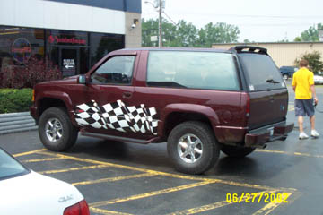 1993 Ford Taurus - Maroon SUV with checkered flag decals parked in a lot next to a white car.