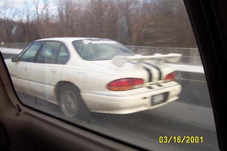 1993 Ford Taurus - A white sedan with a prominent rear spoiler and racing stripes is seen from the rear, possibly a 1993 model.