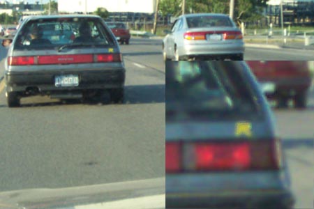 1993 Ford Taurus - A gray hatchback car is seen from the rear on a road, with other vehicles in the background.
