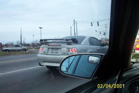 1993 Ford Taurus - A silver coupe with a prominent rear spoiler is seen from the side, with a truck in the background and a date stamp of 02/04/2000.