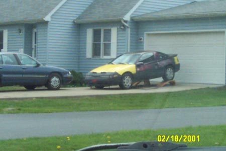 1993 Ford Taurus - A car with a yellow hood and purple body is parked on ramps in front of a garage, with another car to its left.