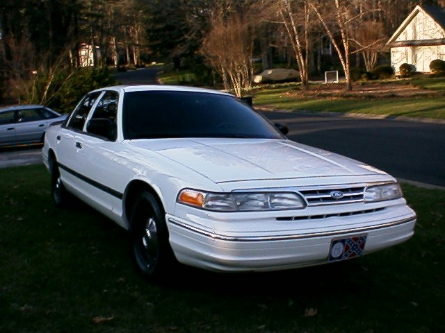 White Ford Crown Victoria sedan, front 3/4 view, black wheels, parked on grass