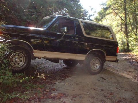 1990 Ford Bronco - This 1990 Ford Bronco is shown off-road on a dirt path surrounded by trees.