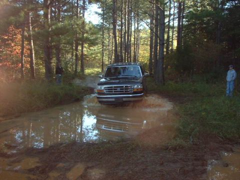 1990 Ford Bronco - This 1990 Ford Bronco is navigating a muddy trail in a forest setting.