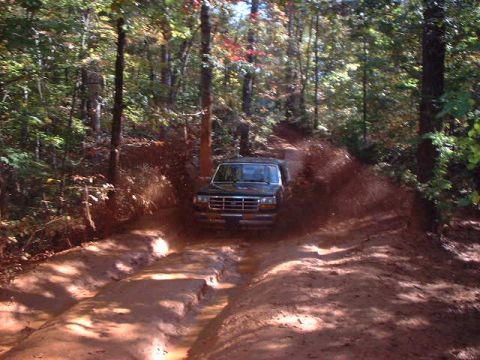 1990 Ford Bronco - A black Ford Bronco navigates a muddy trail through a forest.