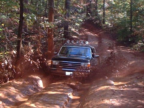 1990 Ford Bronco - This 1990 Ford Bronco navigates a challenging muddy path through a dense forest.