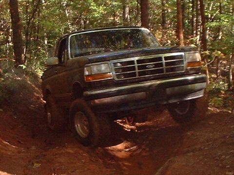 1990 Ford Bronco - A dark-colored Ford Bronco navigates a muddy, wooded trail.