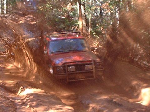 1990 Ford Bronco - SUV navigating a challenging muddy off-road course.