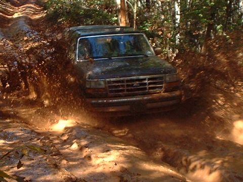 1990 Ford Bronco - A Ford Bronco navigates a muddy trail, sending dirt and water flying.