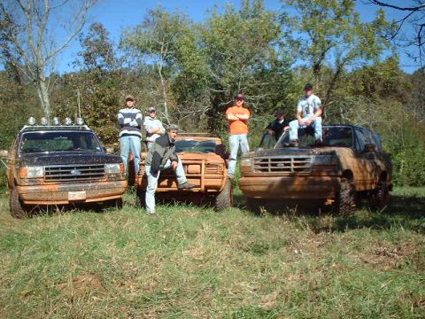 1990 Ford Bronco - A group of people pose with three muddy Ford Broncos in a wooded area.