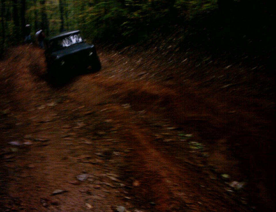 Dark SUV climbing a steep rutted clay trail in the woods, blurry low-light photo