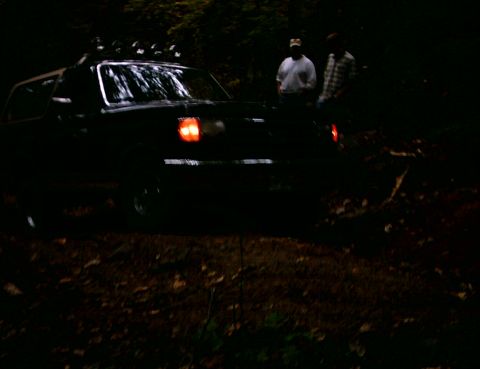 1990 Ford Bronco - A black SUV with roof lights is seen in a wooded area at dusk.