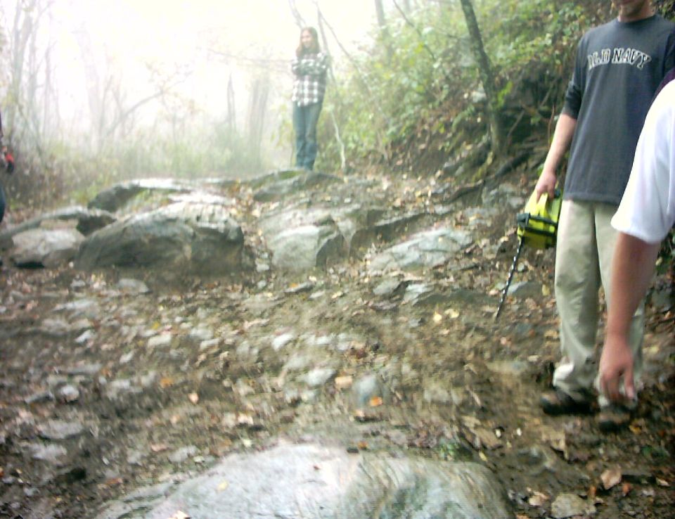 People standing on a foggy, rocky off-road trail with wet boulders and leaves